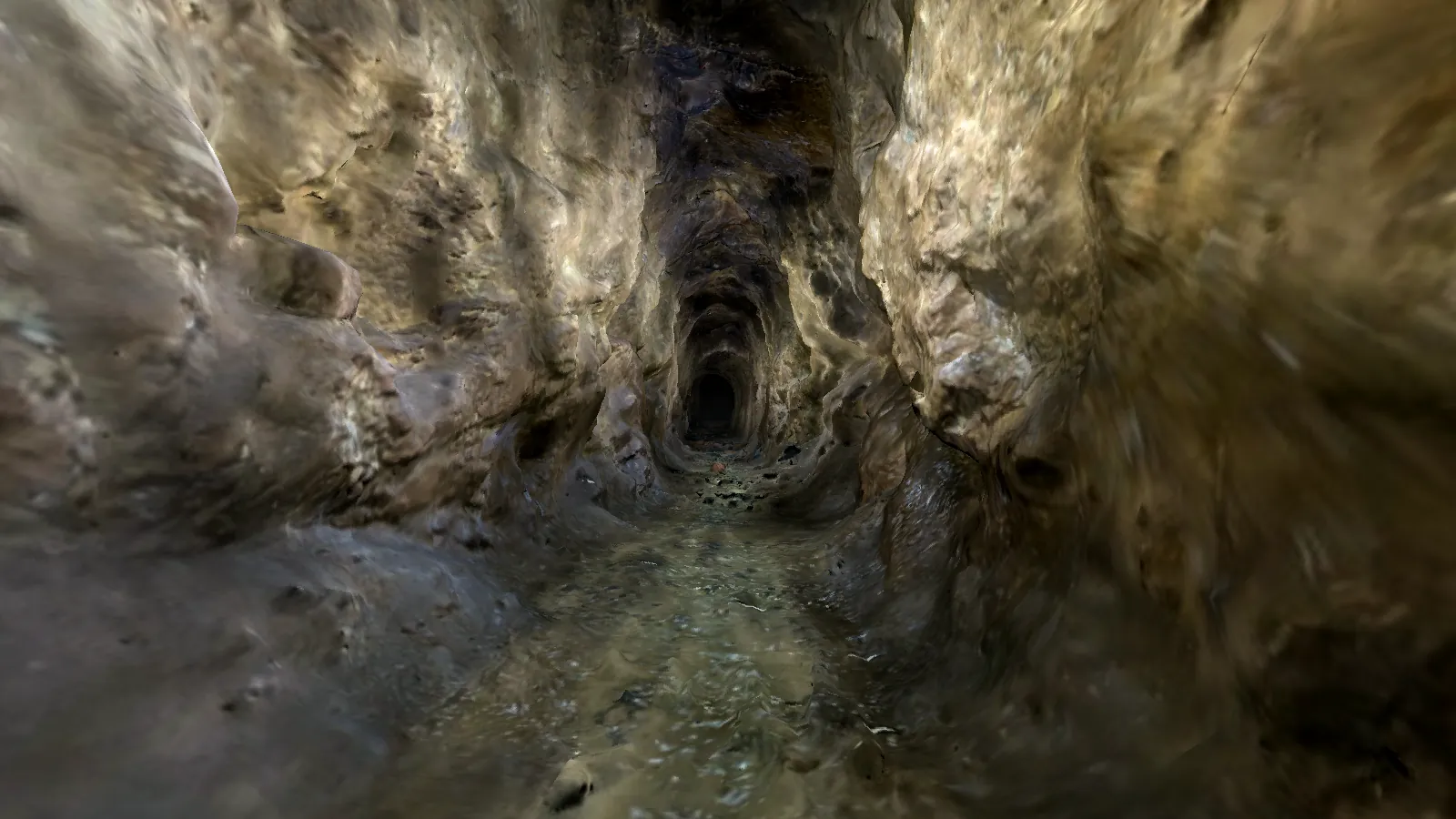A narrow rock tunnel with water on the floor, narrowing further into the distance